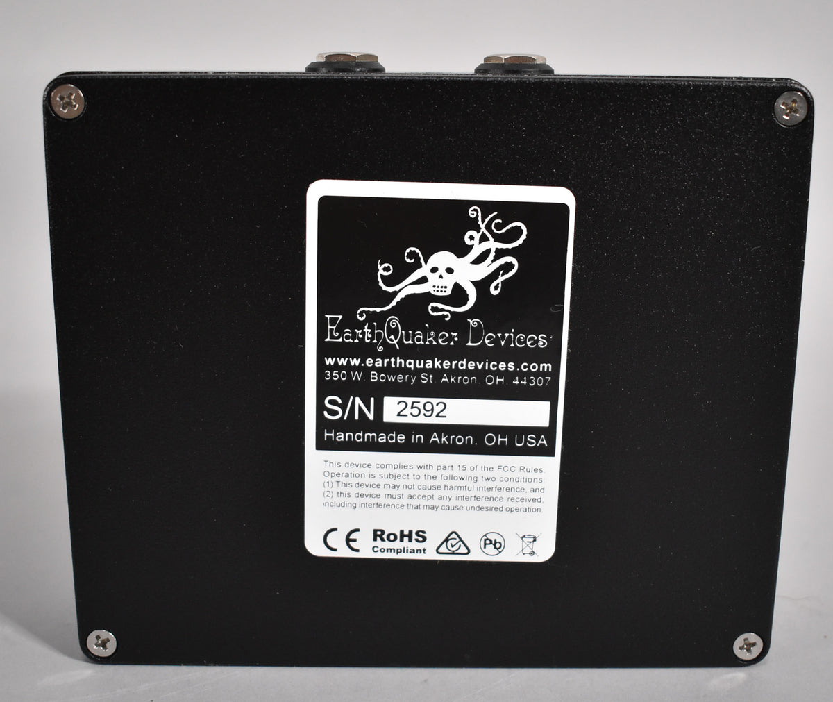 The pedal's textured black underside is shown, with a white label centered and four silver Phillips head screws in the corners.