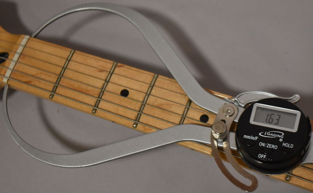 A digital caliper measures the maple fretboard and frets, displaying "1.63" on its screen.