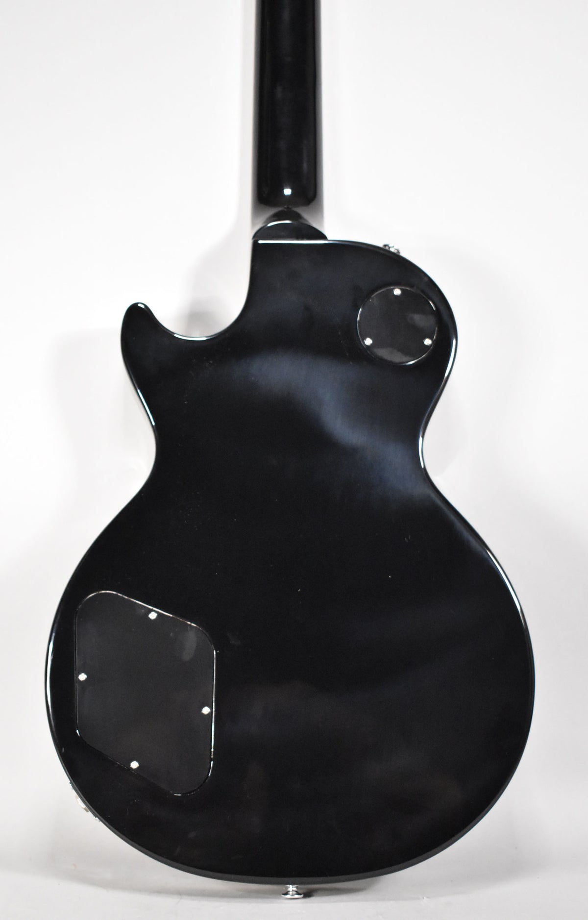 Full back view of the glossy black Les Paul, showing the neck joint, two control cavity covers, and a strap button at the bottom.