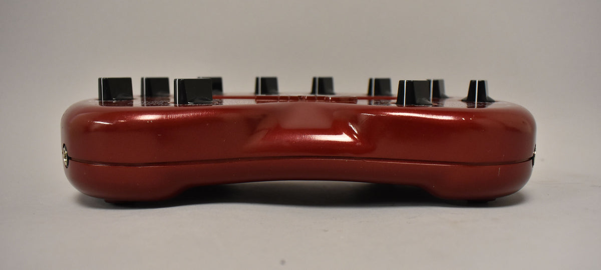 The red, kidney-bean-shaped multi-effects unit is viewed from the side, showing a row of black knobs along its top edge.