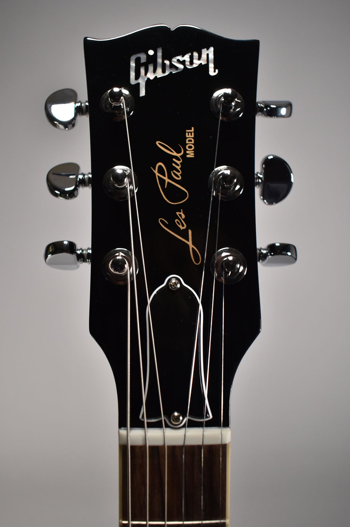 The guitar's glossy black headstock, with chrome tuners and a white nut, is viewed from the front, showing the top of the fretboard.