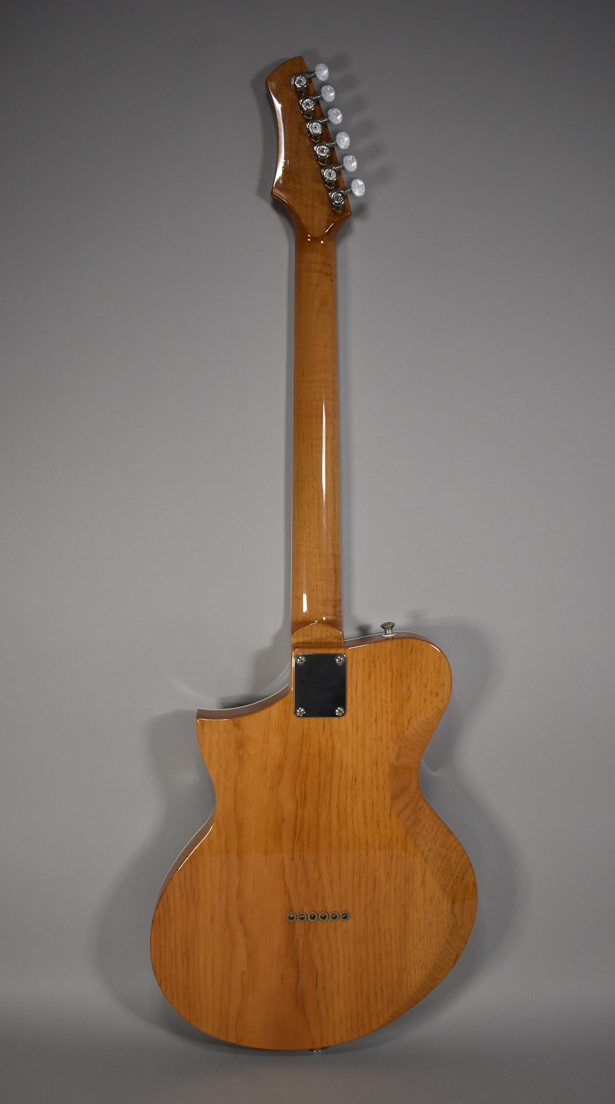 Full rear view of a light brown guitar with a glossy finish, showing the neck joint, six string ferrules, and white tuning pegs.