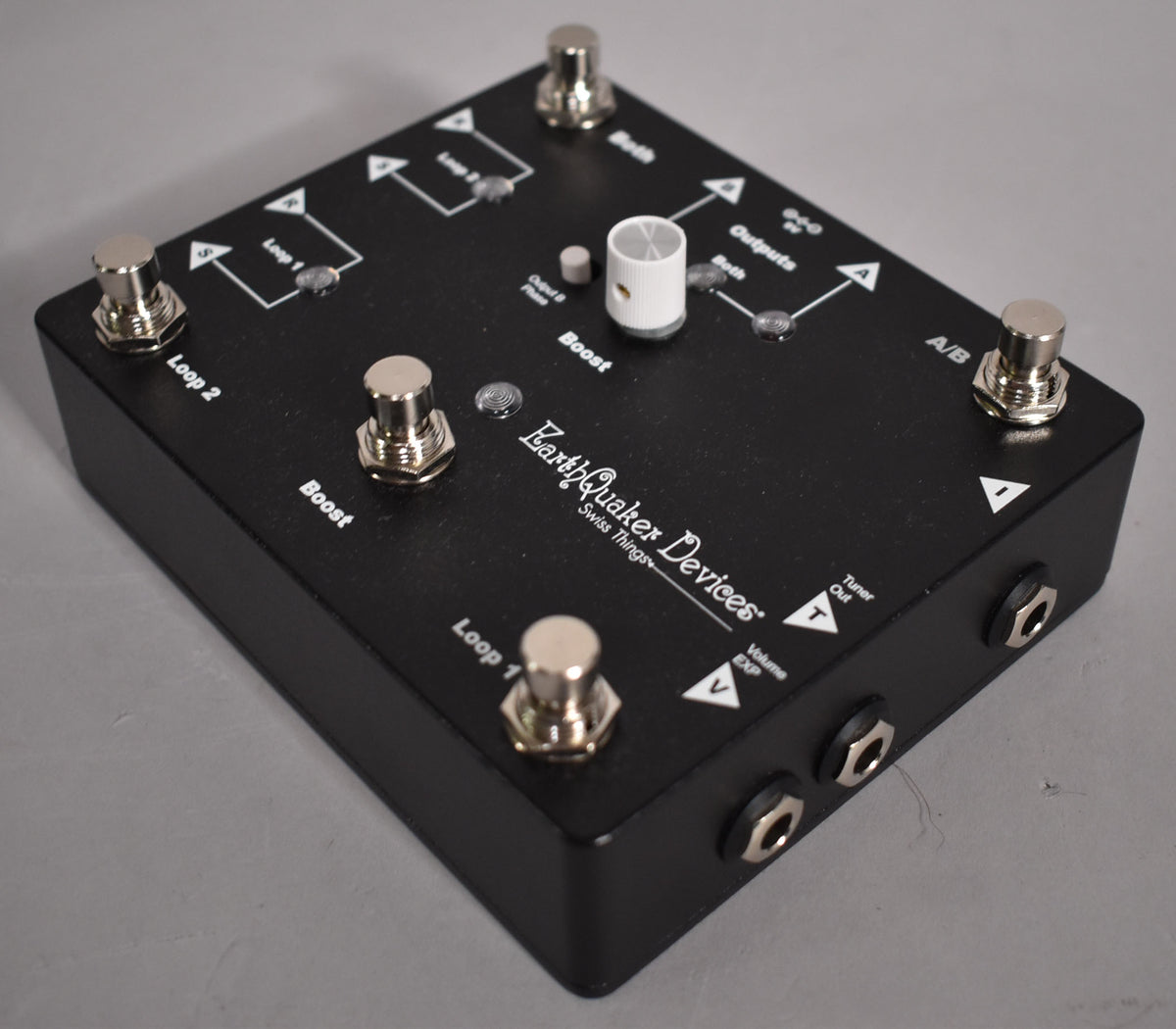 A black pedal with a textured finish, viewed from above and angled right, showing five chrome footswitches and a white knob.