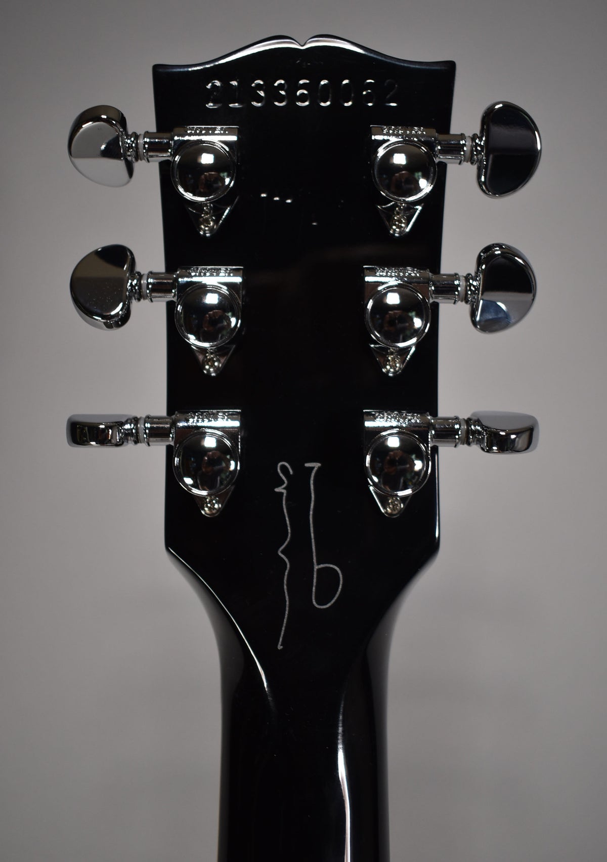 Rear view of the glossy ebony headstock and neck, showing six chrome tuners and a white etched signature.
