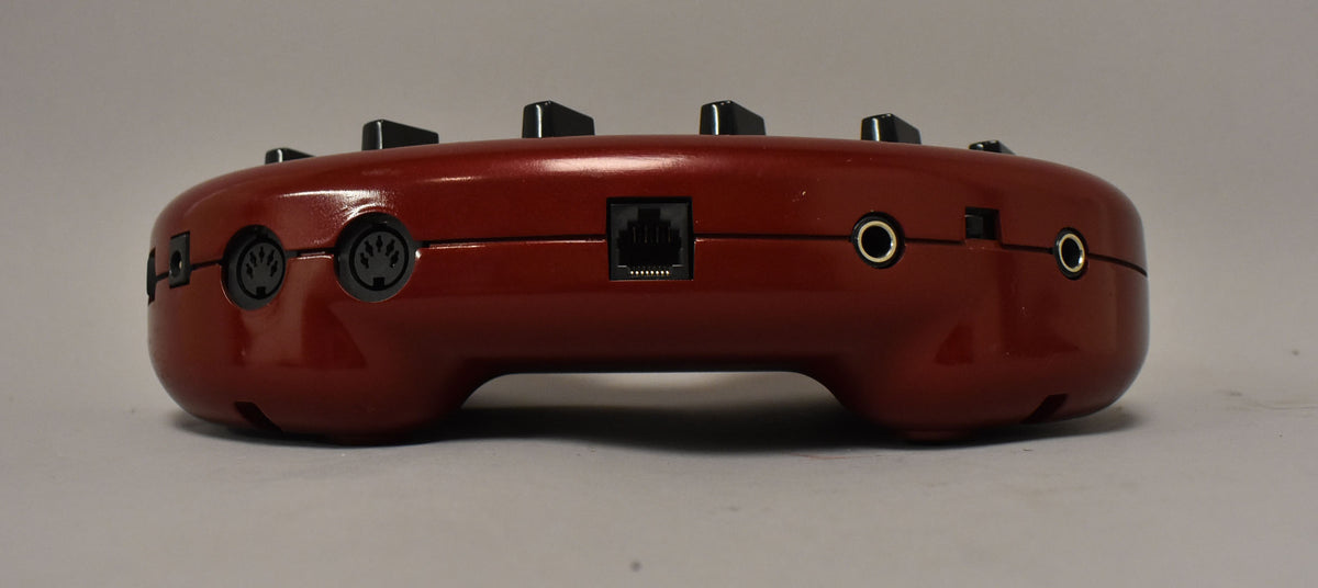 The Line6 POD 2.0's glossy red, kidney-bean-shaped body is seen from the rear, showing two MIDI ports, an ethernet port, and two audio jacks.