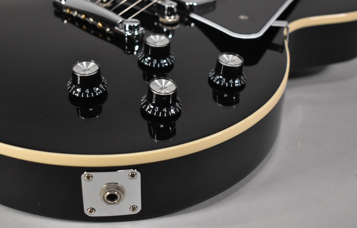 Close-up of the guitar's lower bout, showing the glossy black finish, cream binding, four black control knobs, and chrome output jack.