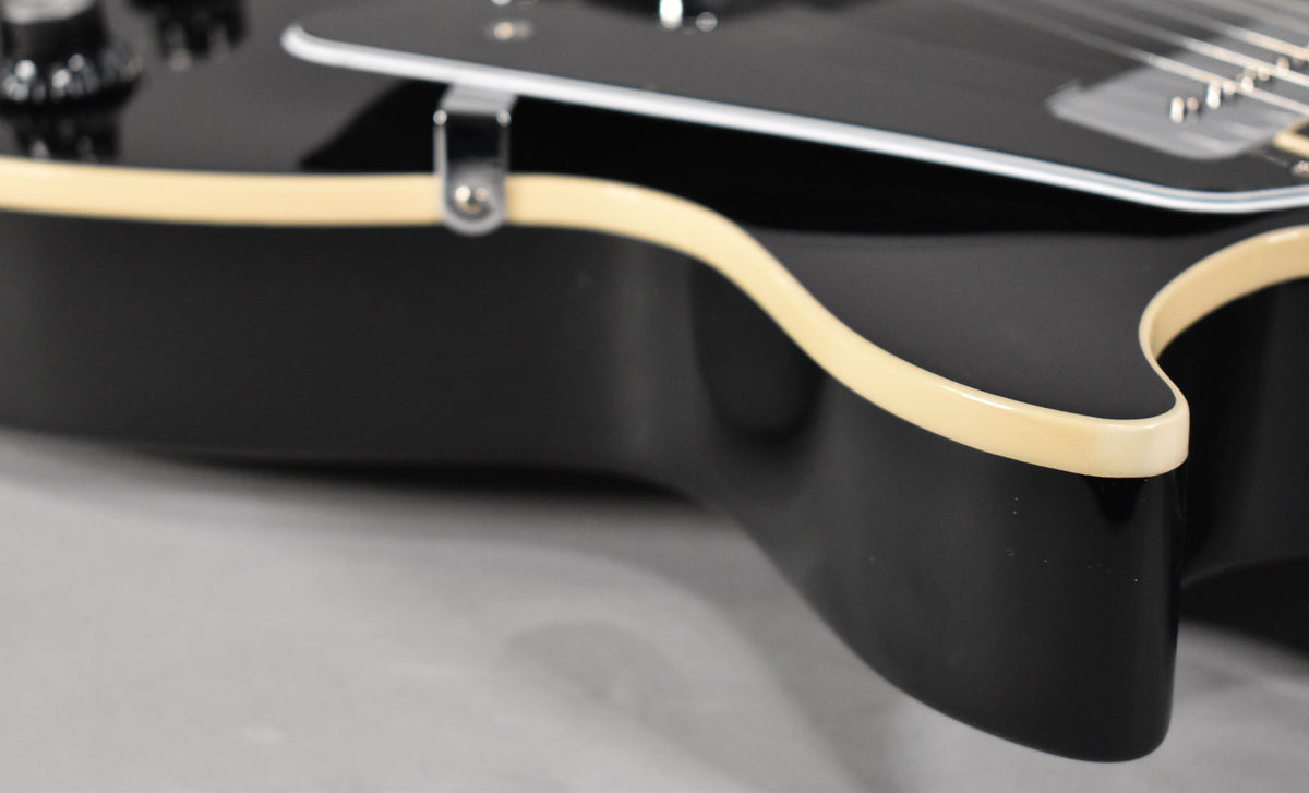 Close-up of the guitar's lower bout, showing the glossy black finish and cream binding, with a hint of the pickguard.