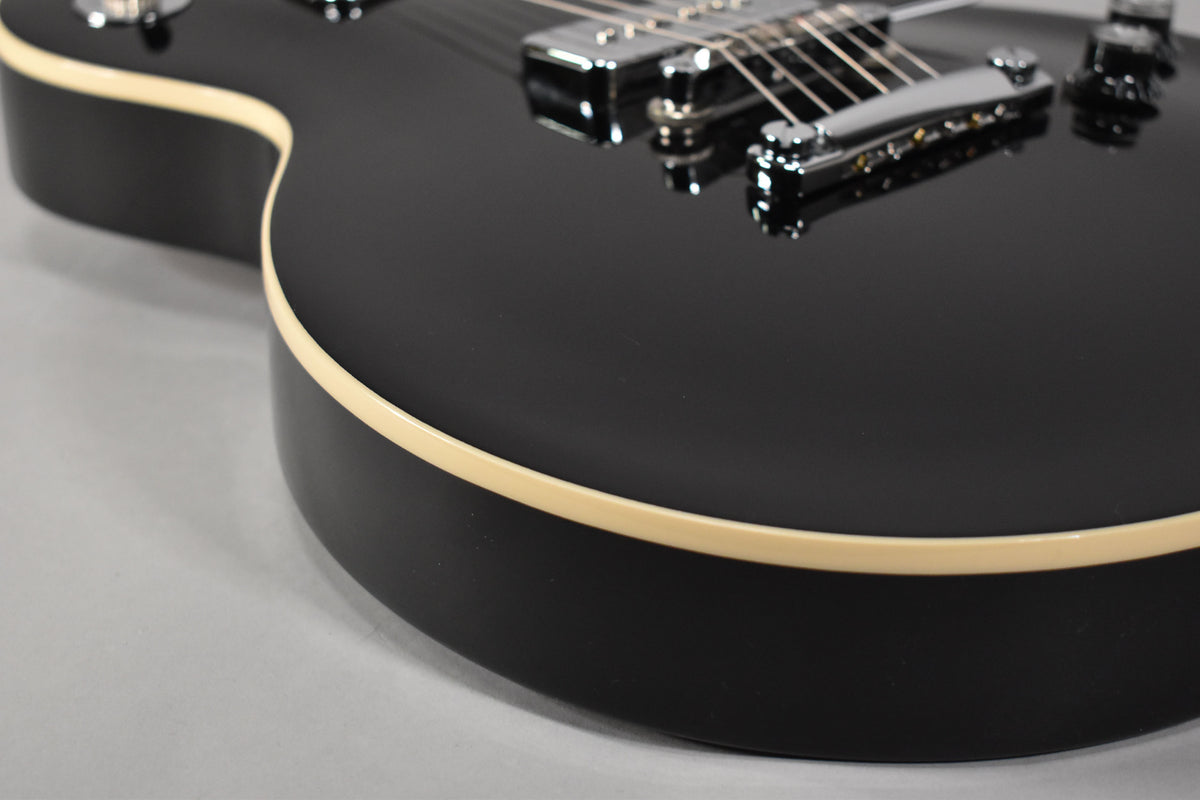 Close-up of the guitar's lower bout, showing the glossy black finish, cream binding, and chrome bridge and tailpiece.