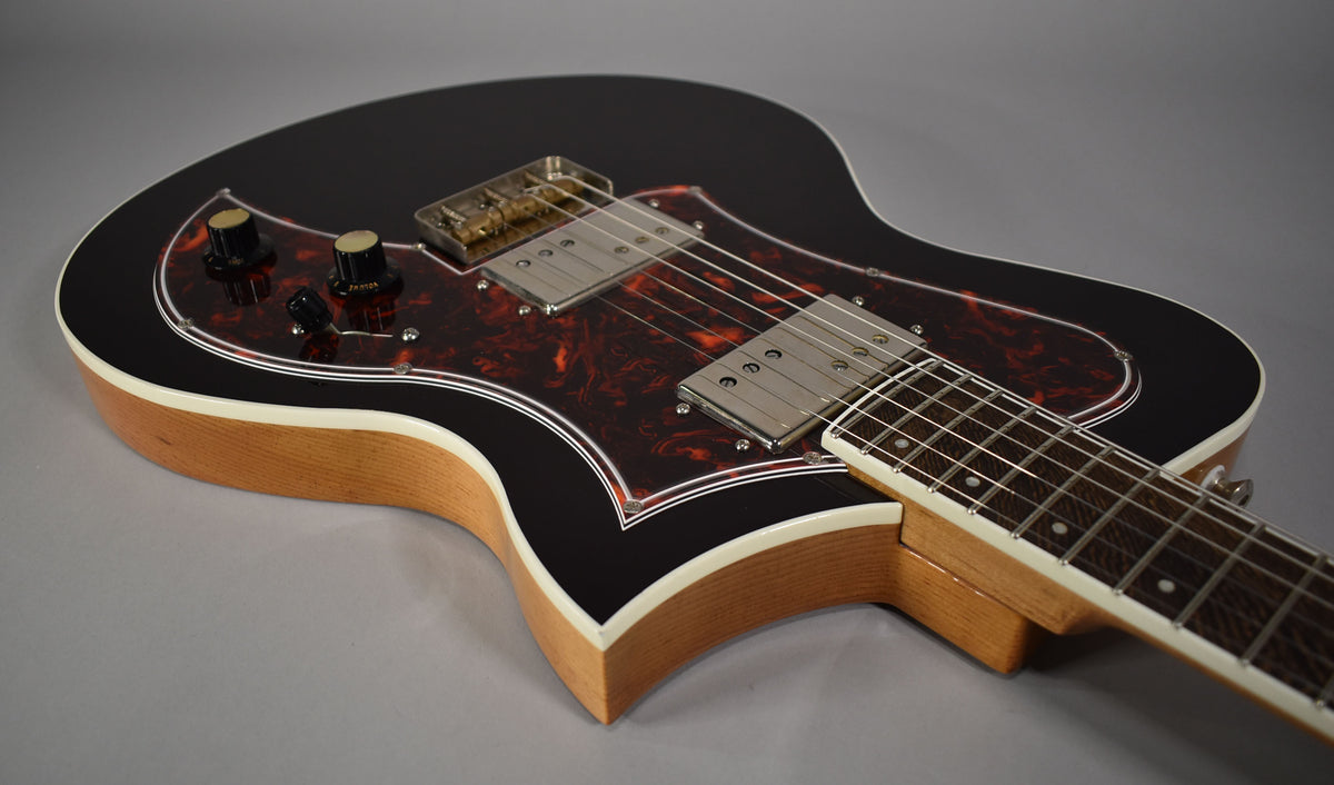 A black guitar with a tortoiseshell pickguard, two humbuckers, and a light wood body with white binding.