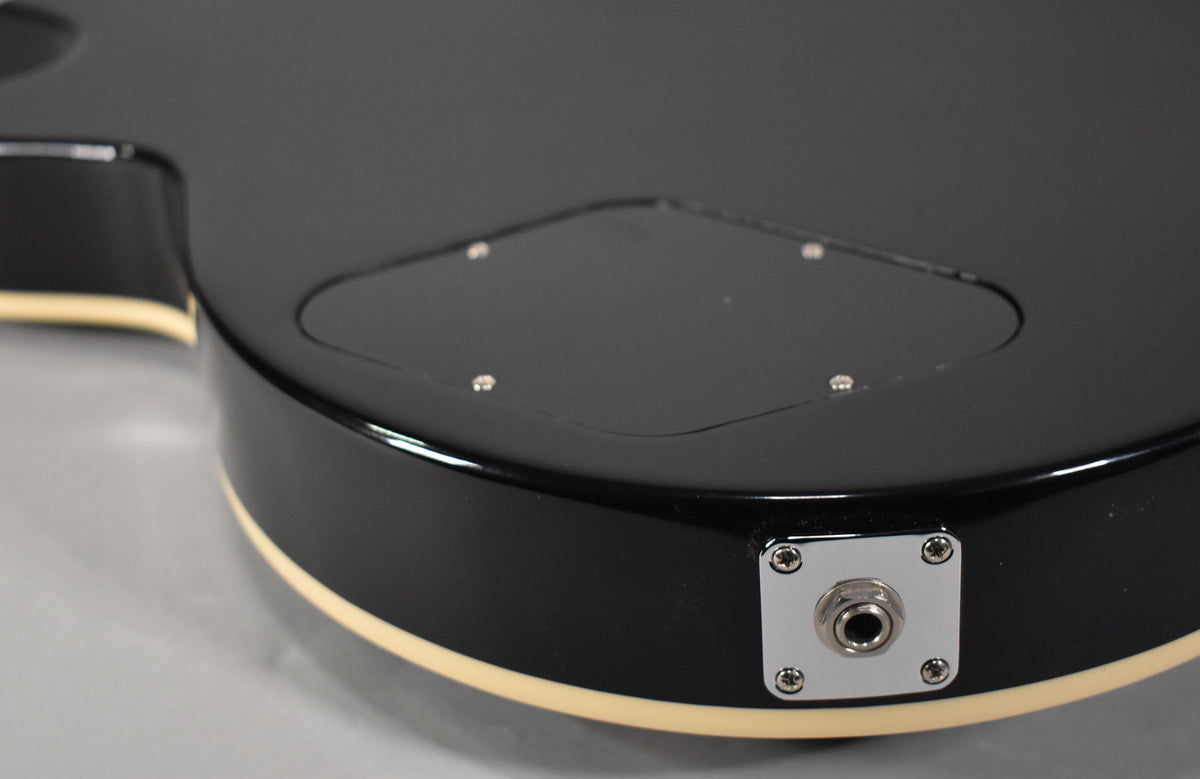 Close-up of the guitar's lower bout, showing the glossy black finish, cream binding, chrome output jack, and control cavity cover.