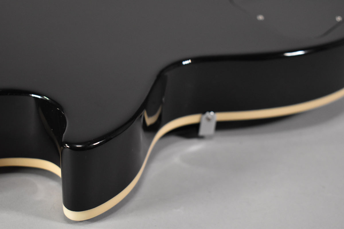 Close-up of the lower bout of the ebony Les Paul, showing the glossy black finish, cream binding, and a chrome strap button.