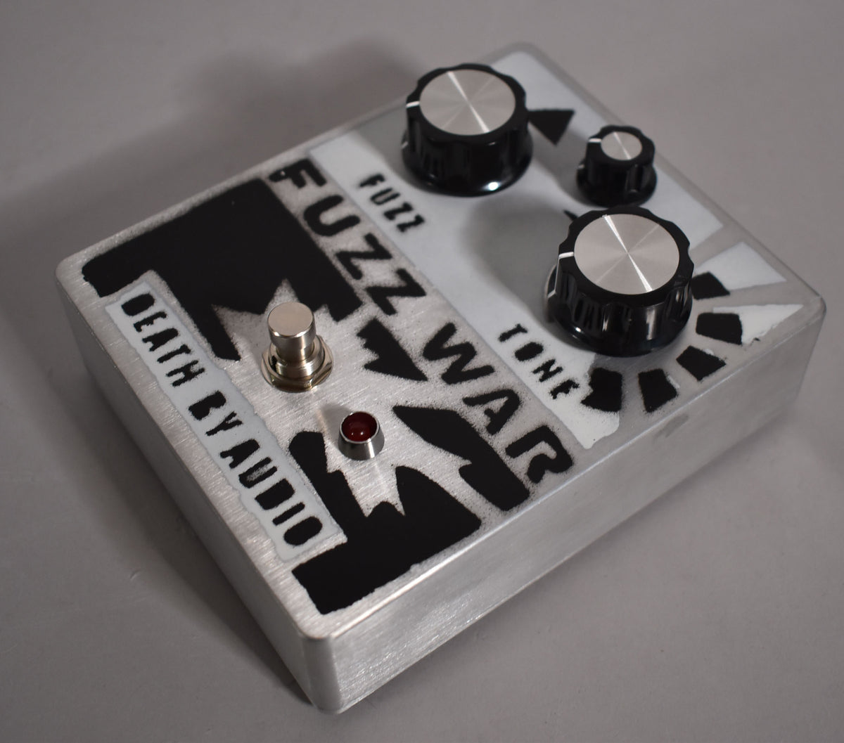 Brushed aluminum pedal with black and white graphic, three black knobs with silver tops, a silver footswitch, and a red LED.