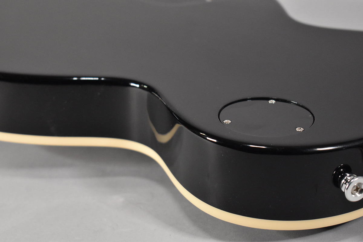 Close-up of the guitar's lower bout, showing the glossy black finish, cream binding, and the circular control cavity cover.