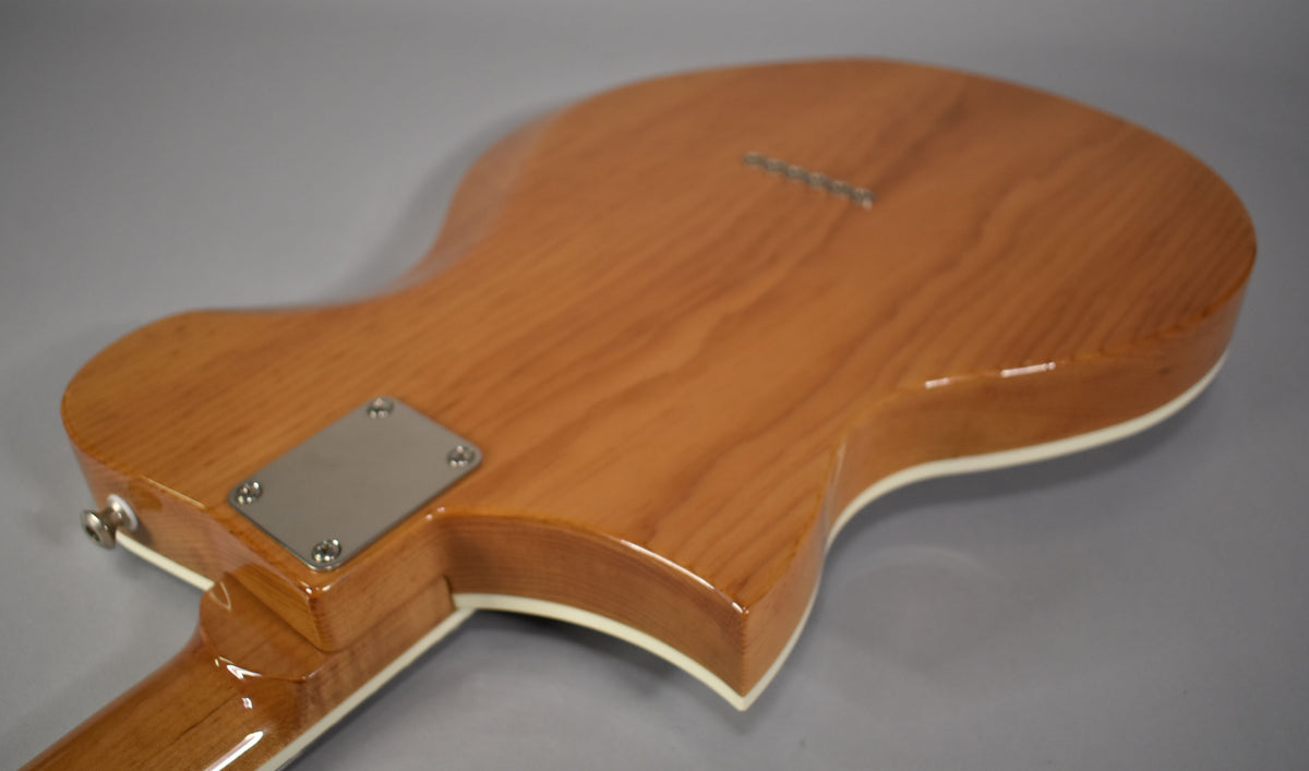 The back of a light brown guitar with a glossy finish, showing a chrome neck plate and string-through-body ferrules.