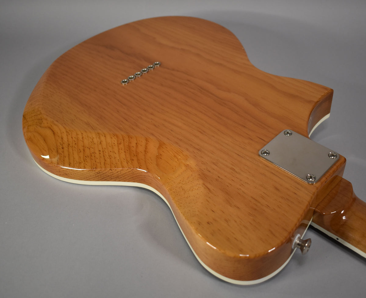 The guitar's glossy natural wood back, with visible grain, shows six string-through-body ferrules and a chrome neck plate.
