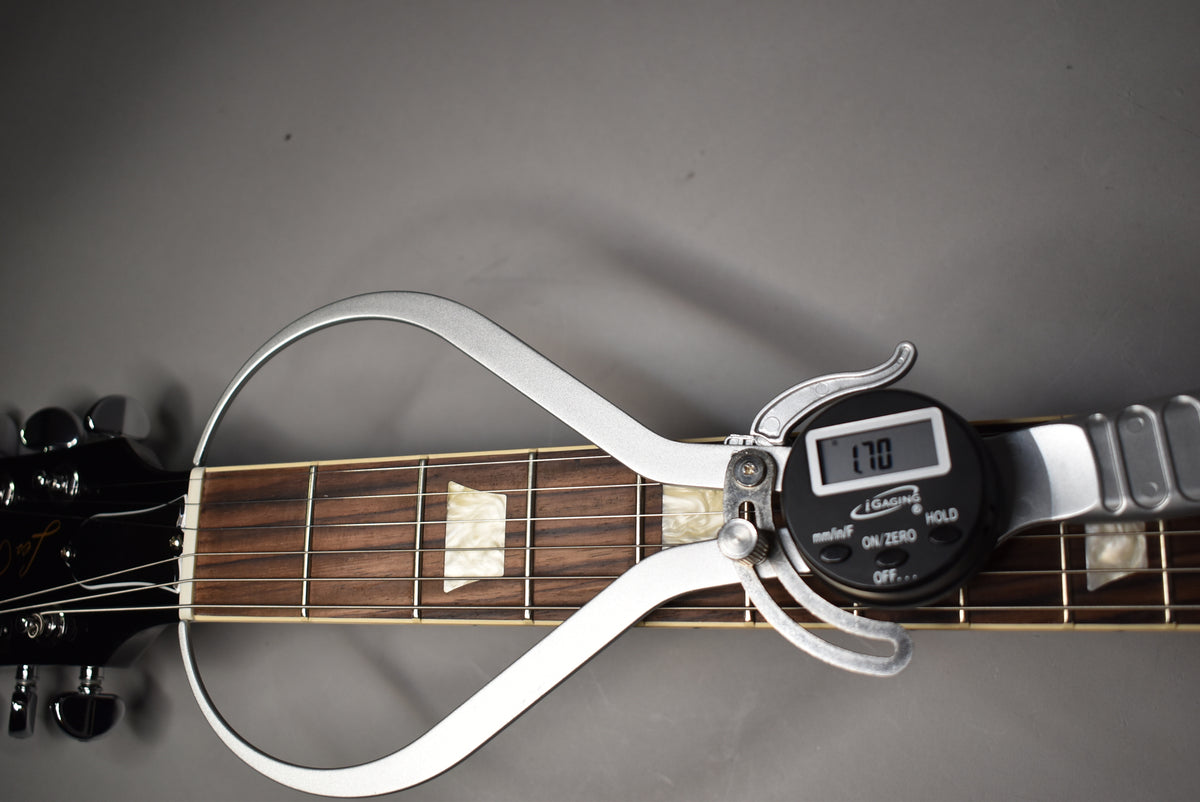 A digital caliper measures the nut width of the ebony Les Paul, showing 1.70 inches, with trapezoid inlays visible on the fretboard.