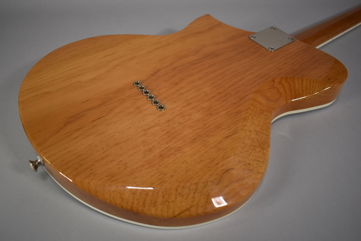 The back of the guitar shows a natural wood finish with visible grain, six string-through-body ferrules, and a chrome neck plate.