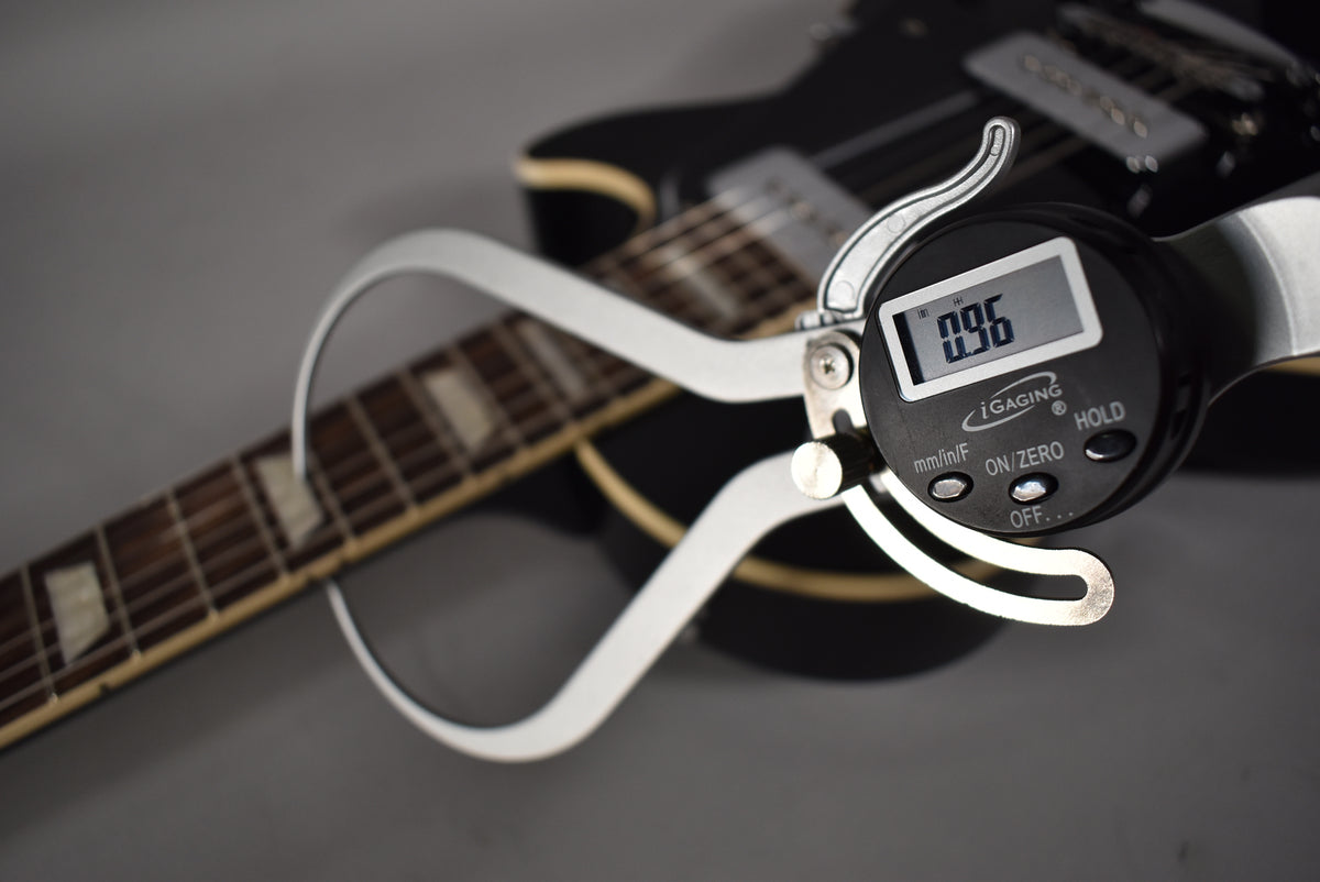 A digital caliper measuring the fret height of the ebony Les Paul's dark rosewood fretboard with trapezoid inlays.