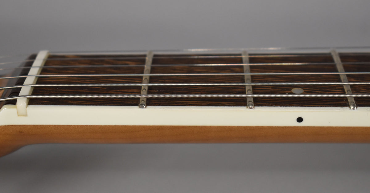 Close-up of the guitar's fretboard, showing dark wood, metal frets, white binding, and a light brown neck, with a single black side dot.