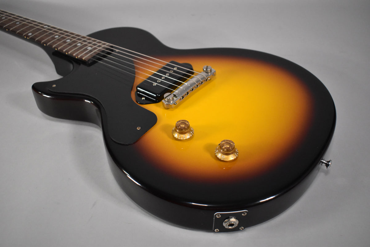 The sunburst Les Paul Junior's body is angled, showing its black pickguard, single P90 pickup, two amber knobs, and output jack.