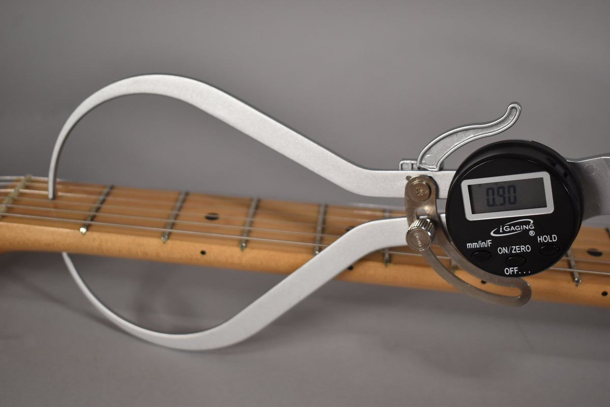A digital caliper measures the maple fretboard and strings, showing a reading of 0.90.