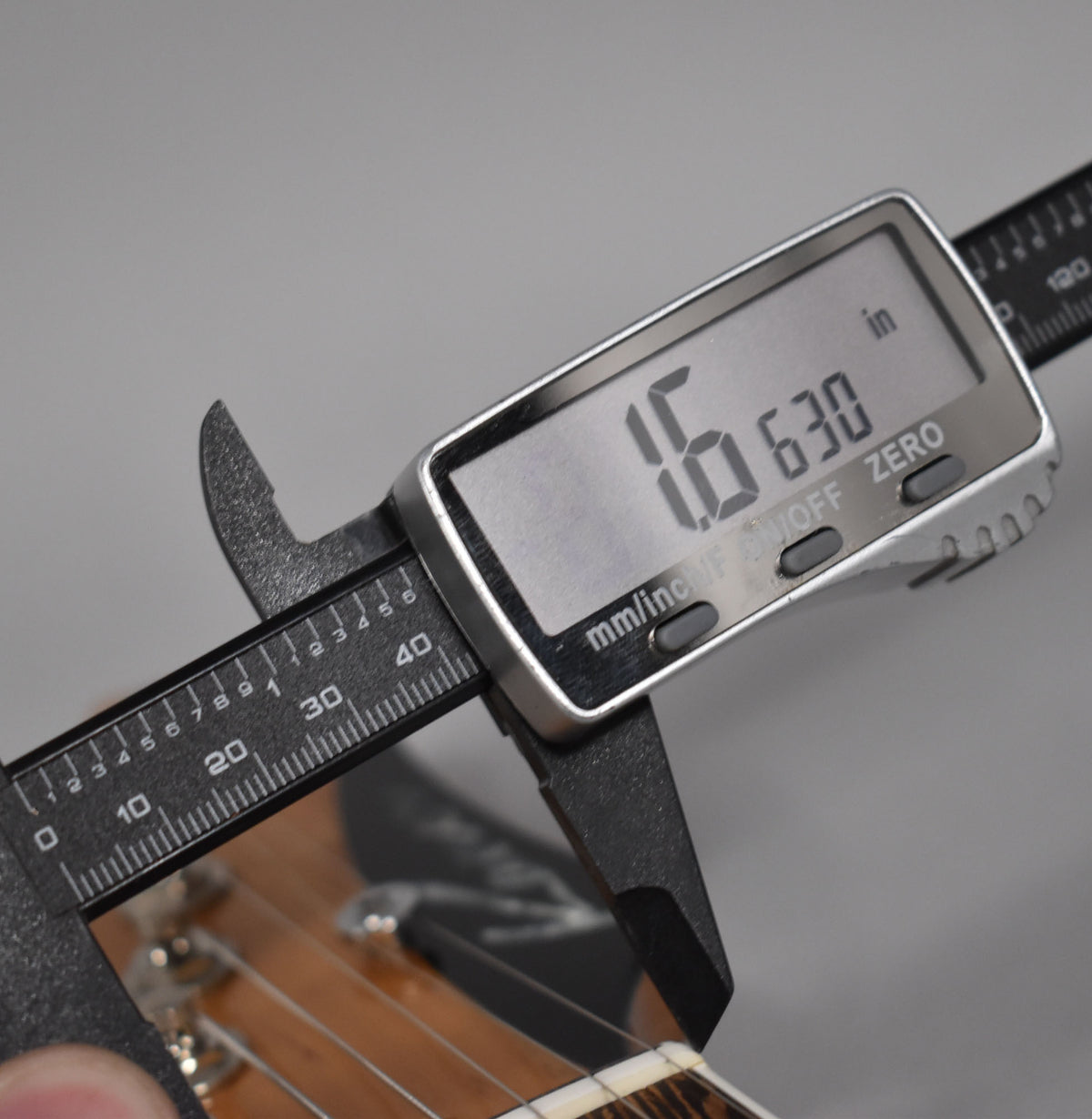 A digital caliper measures the guitar's nut width at 1.630 inches, with the fretboard and strings visible below.