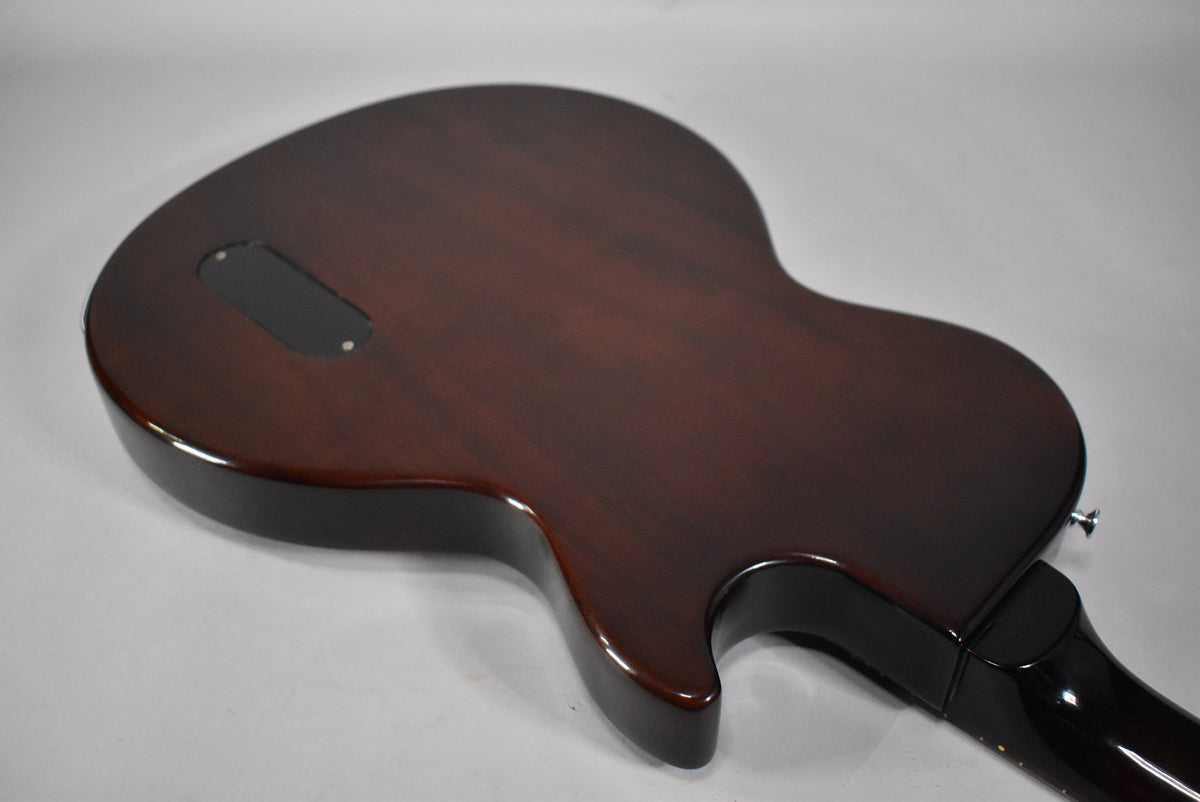 The guitar's dark sunburst back is angled from the upper left, showing a control cavity cover and the neck heel.