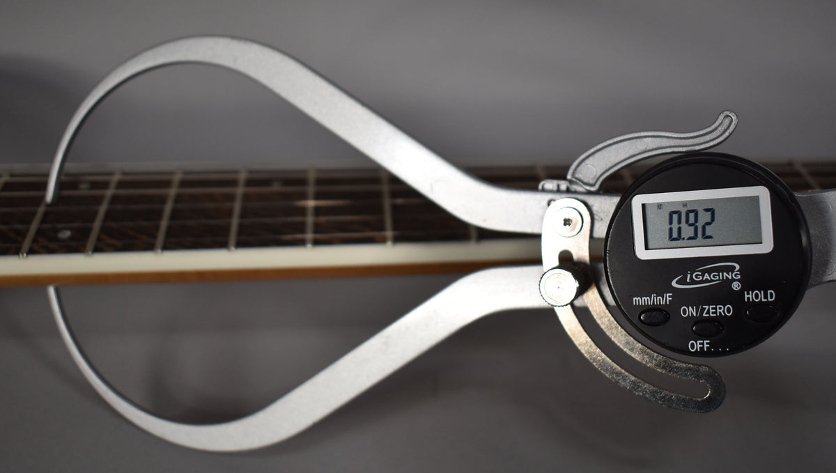 A digital caliper measures the guitar's fretboard, showing a reading of 0.92, with dark frets and light binding visible.