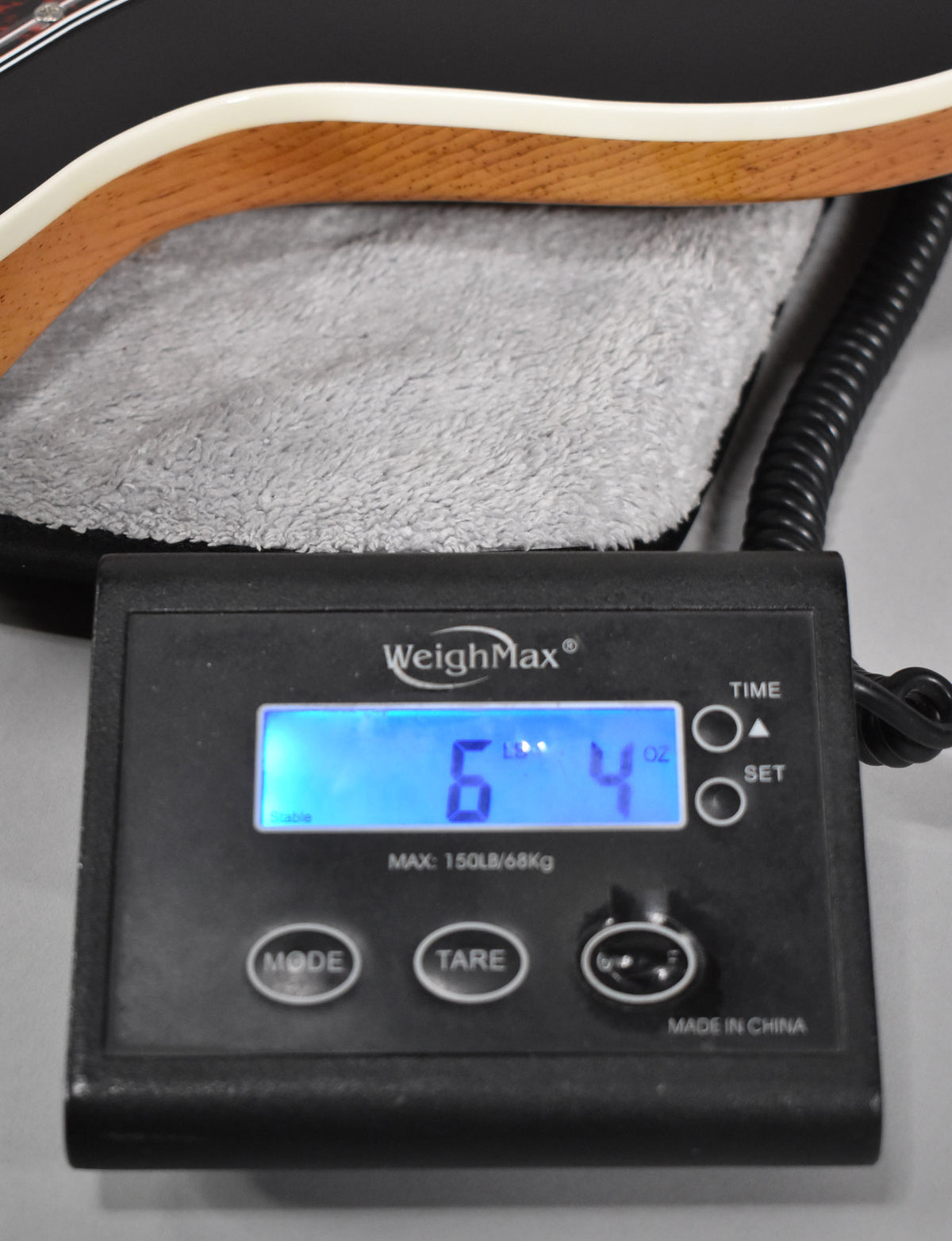 The guitar's oxblood body with cream binding rests on a grey cloth, on a scale displaying "6 Lb 4 Oz".