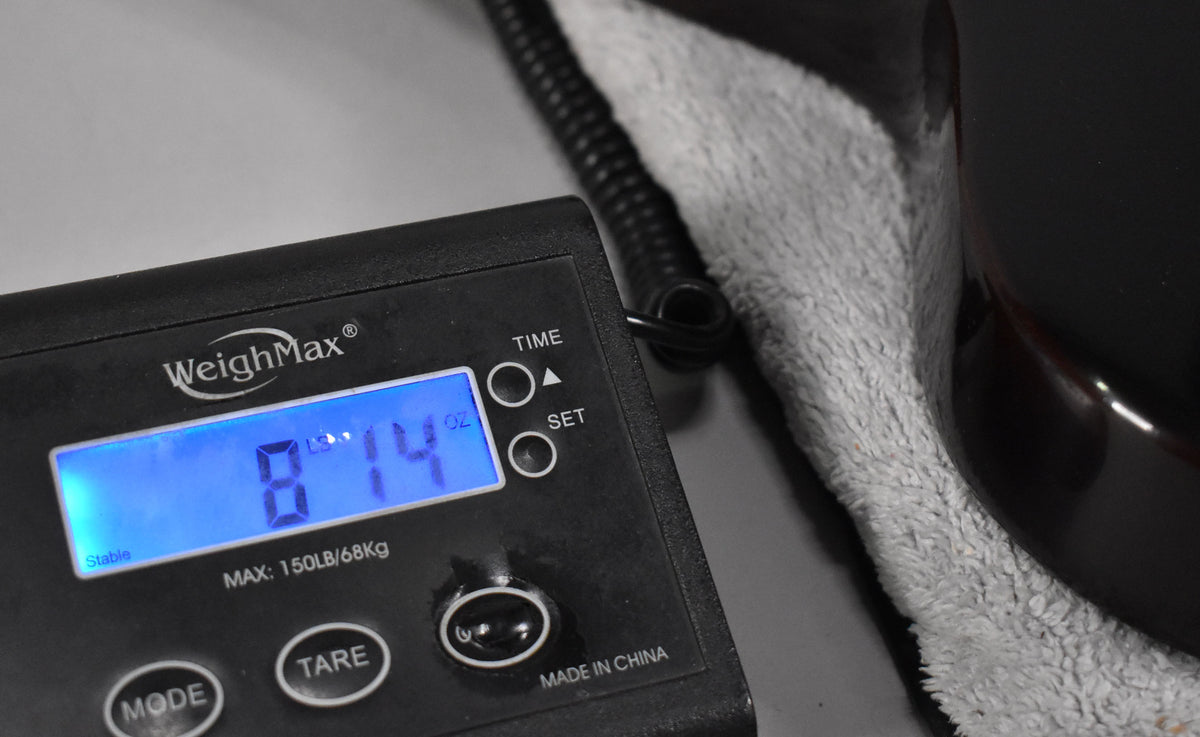 A digital scale displays "8 LB 14 OZ" next to the dark sunburst body of the guitar, resting on a light grey plush lining.