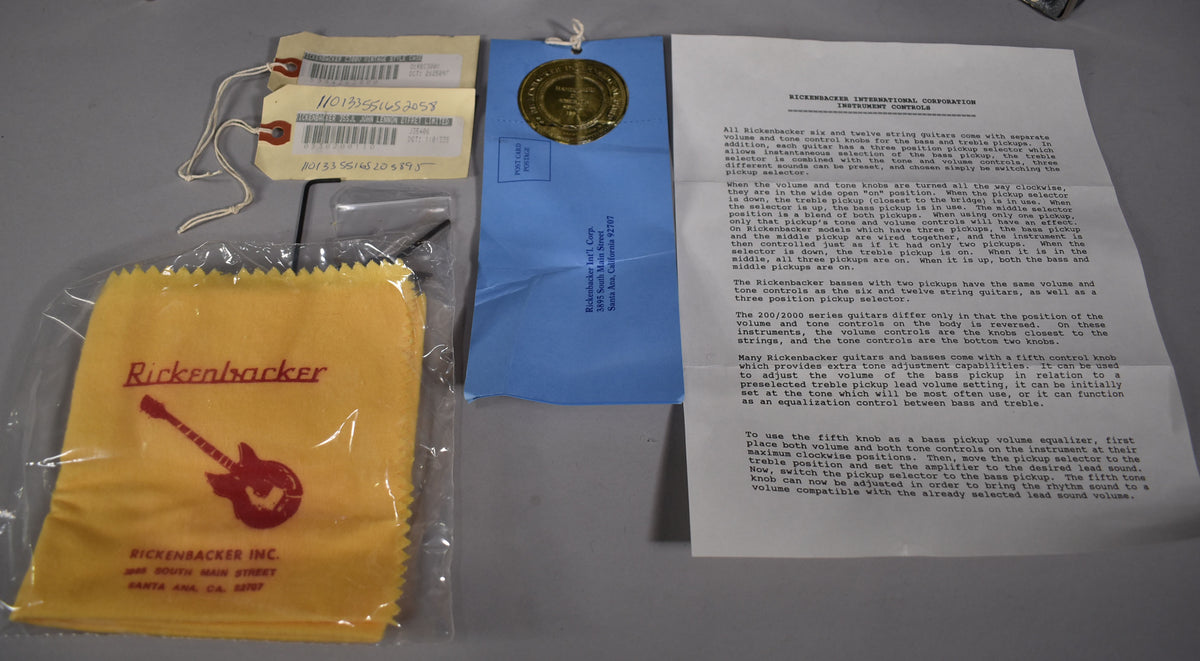 This overhead shot shows two hang tags, a blue envelope with a gold seal, a yellow polishing cloth, and a white instruction sheet.
