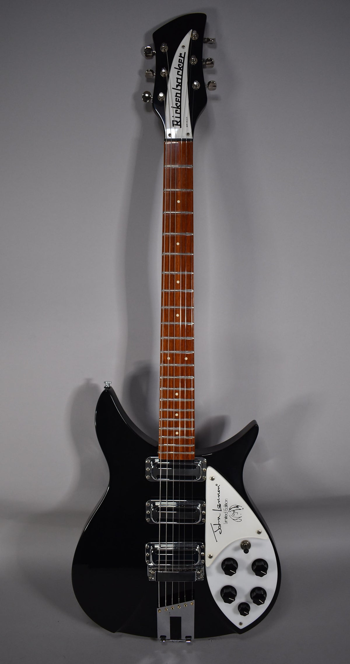 A full-length shot of a black Rickenbacker guitar with a white pickguard signed "John Lennon Limited Edition".