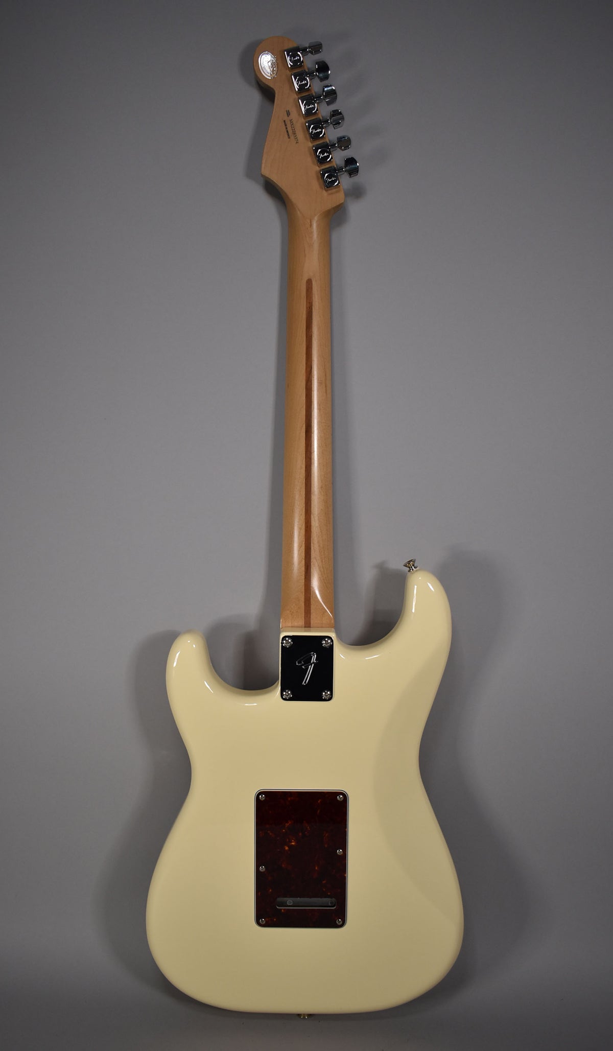The back of an Olympic White Stratocaster, showing the maple neck, chrome tuners, and a tortoiseshell tremolo cover.