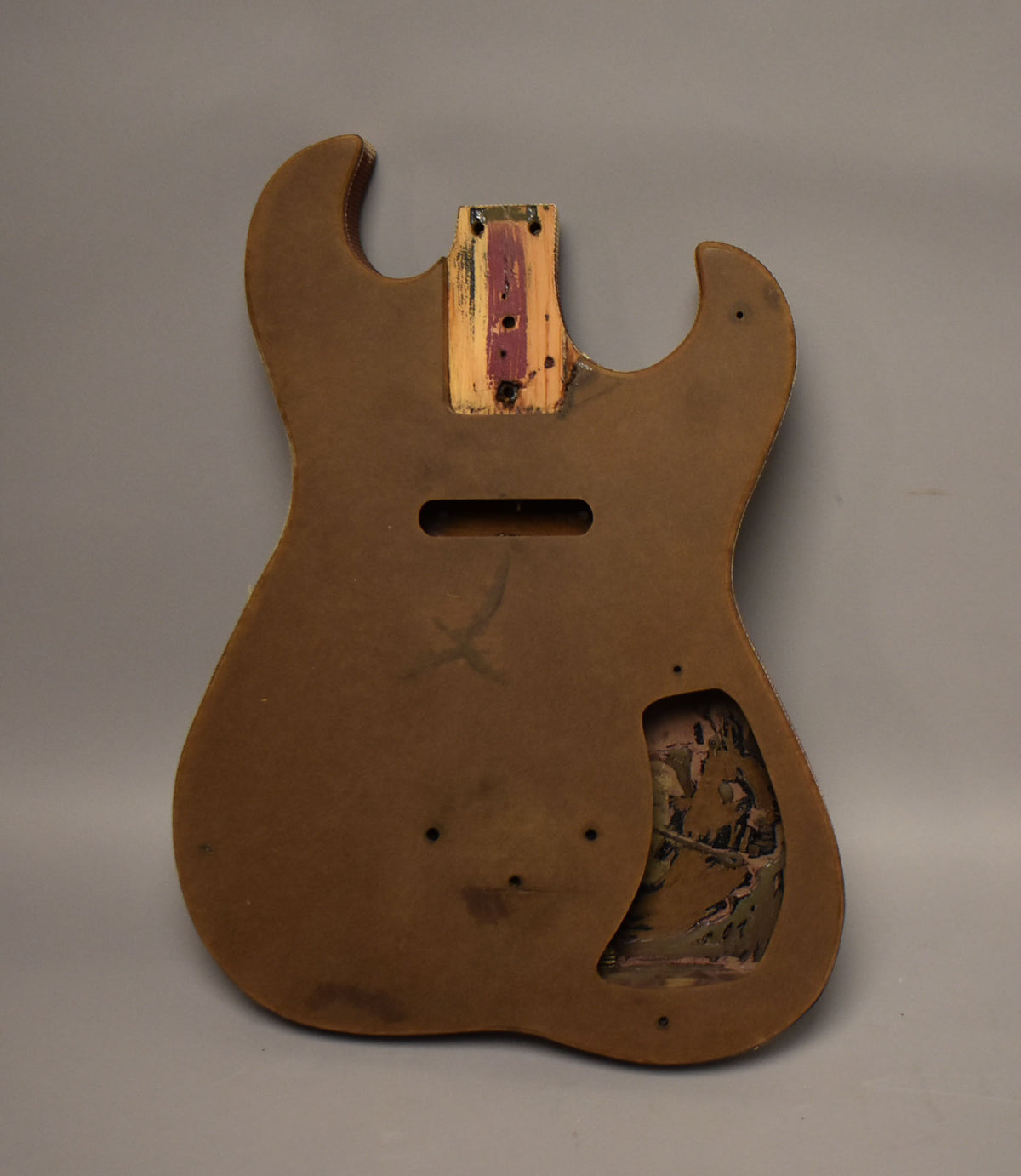 Rear view of a brown guitar body with a neck pocket, pickup route, and control cavity showing chipped paint.