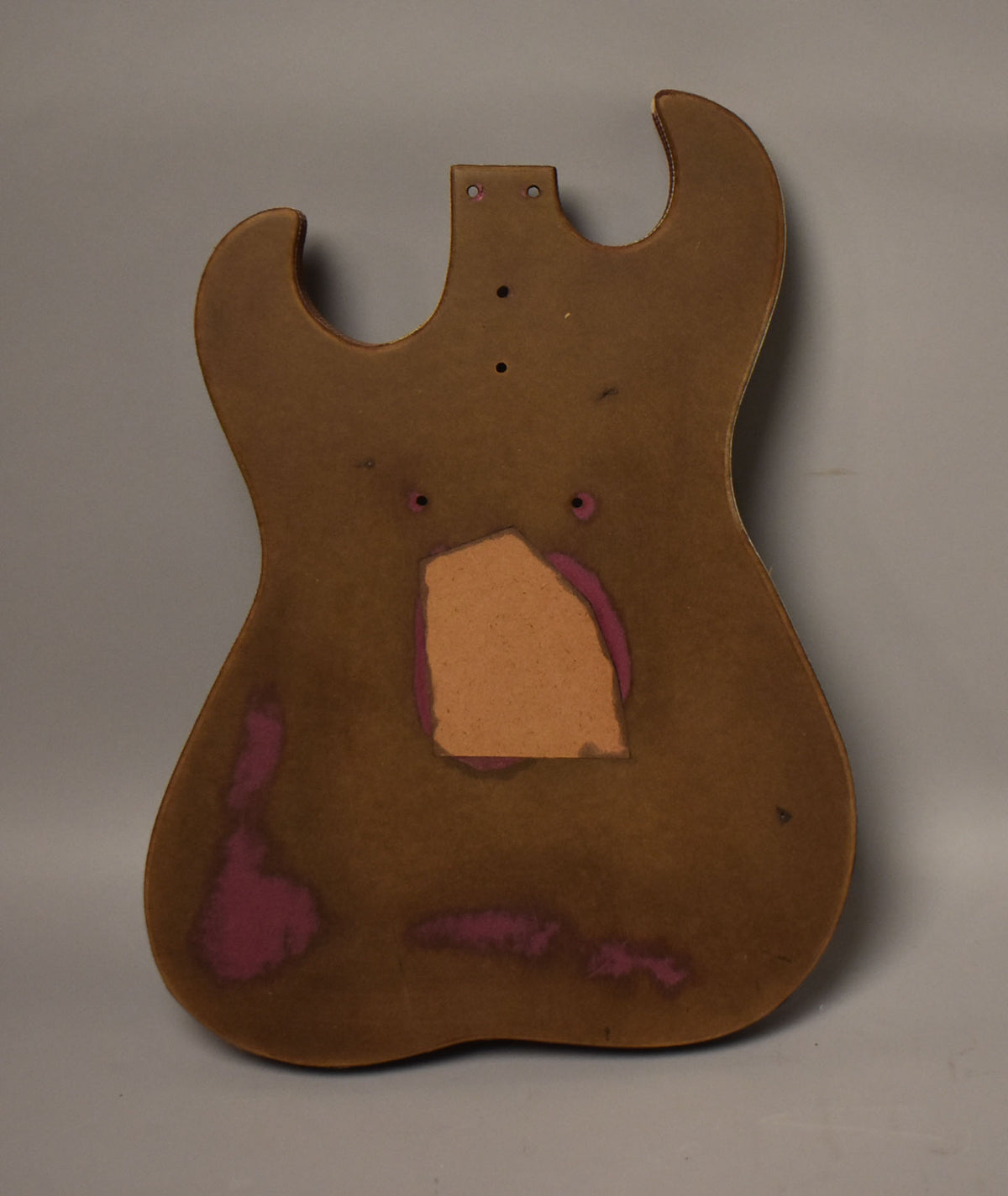 Full view of a brown guitar body with a large rectangular cutout and purple residue, plus several screw holes.