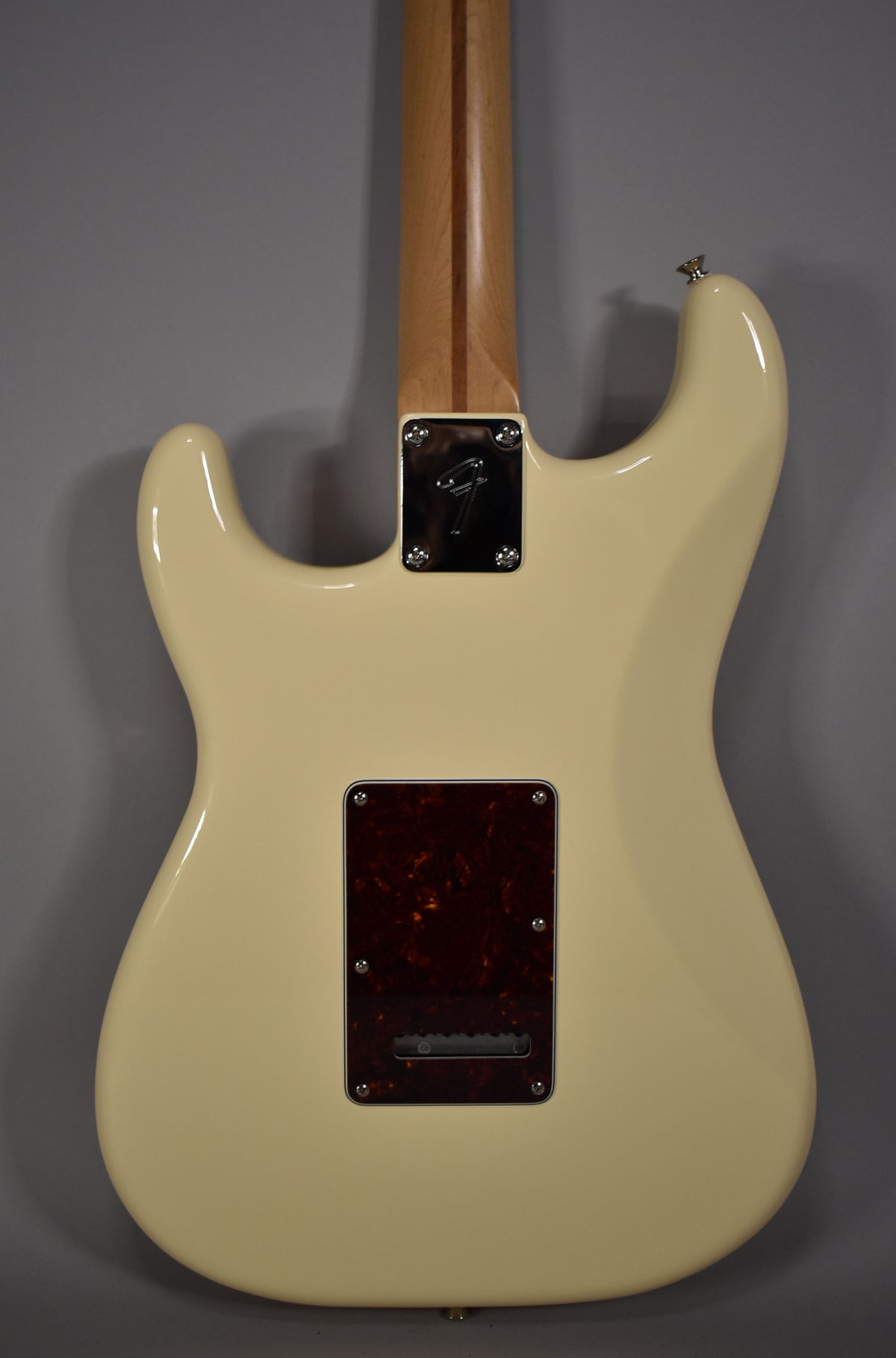 Rear view of an Olympic White Stratocaster body, showing the neck joint, a tortoiseshell tremolo cover, and a light maple neck.