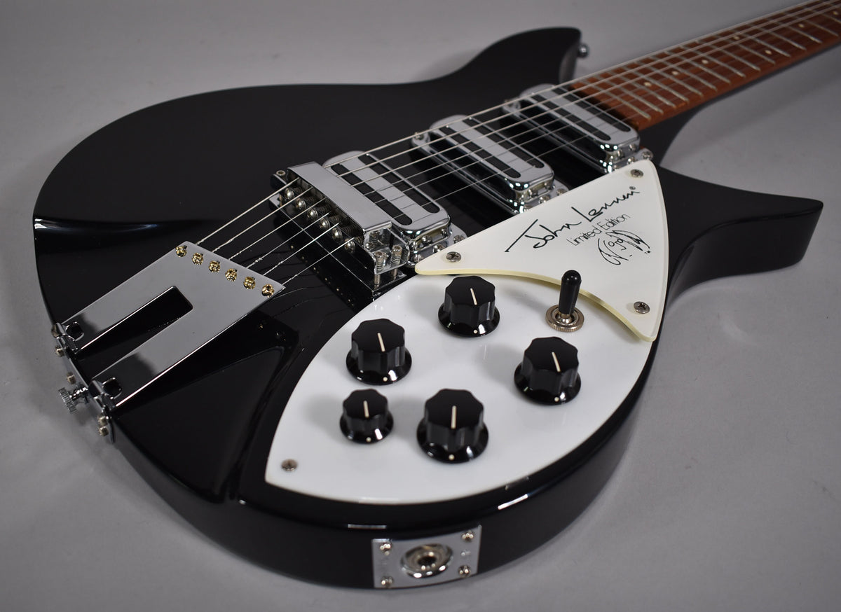 Close-up of a black Rickenbacker guitar with a white pickguard signed "John Lennon Limited Edition", showing the bridge, pickups, and controls.