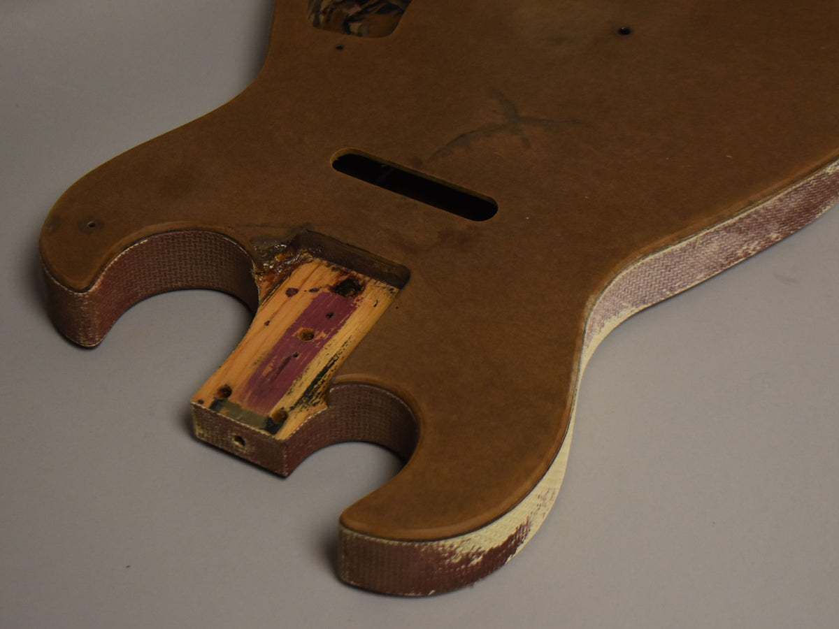 The brown guitar body, viewed from above, shows a worn white finish on the lower bout and a damaged neck pocket with exposed wood.