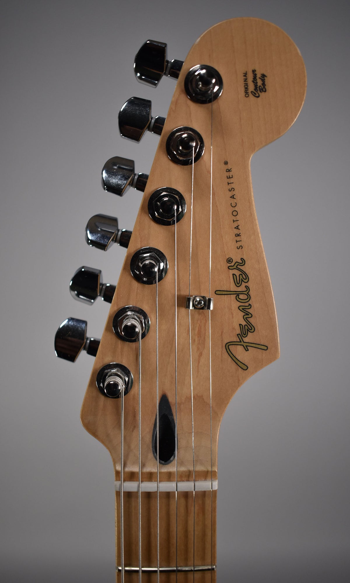 Close-up of a light wood Stratocaster headstock with six chrome tuners, a string tree, and a black truss rod access hole.