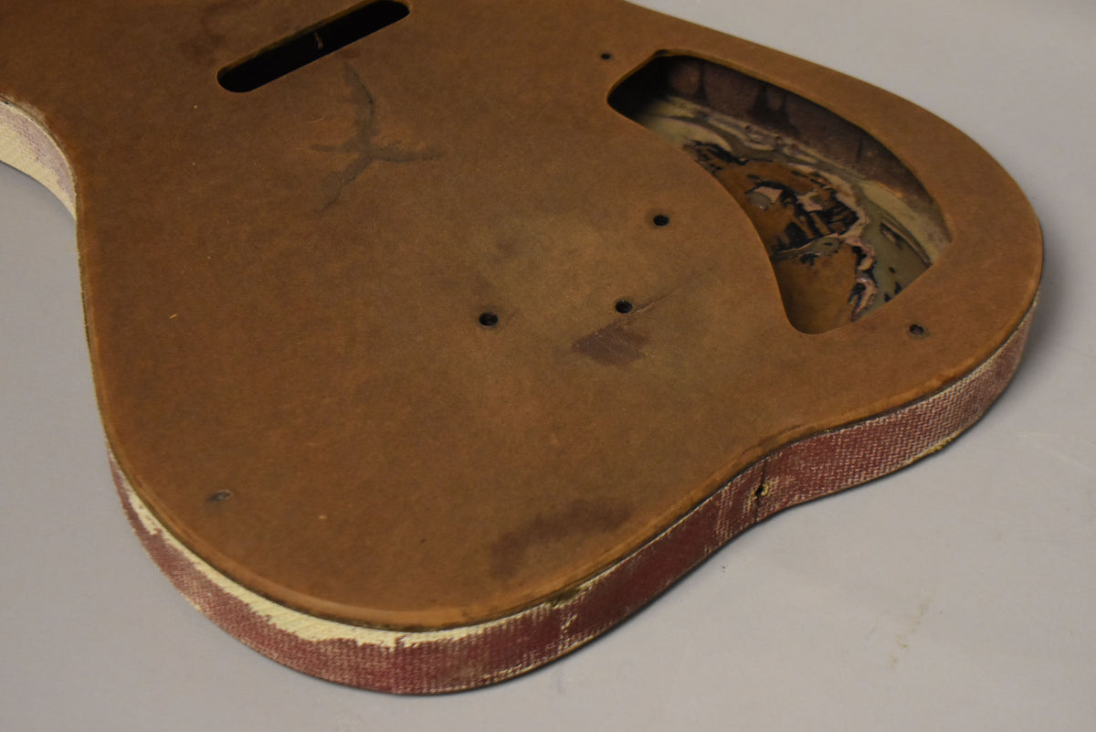 The guitar body, angled from above, shows a worn brown top, red fabric sides, and a large control cavity with peeling paint.