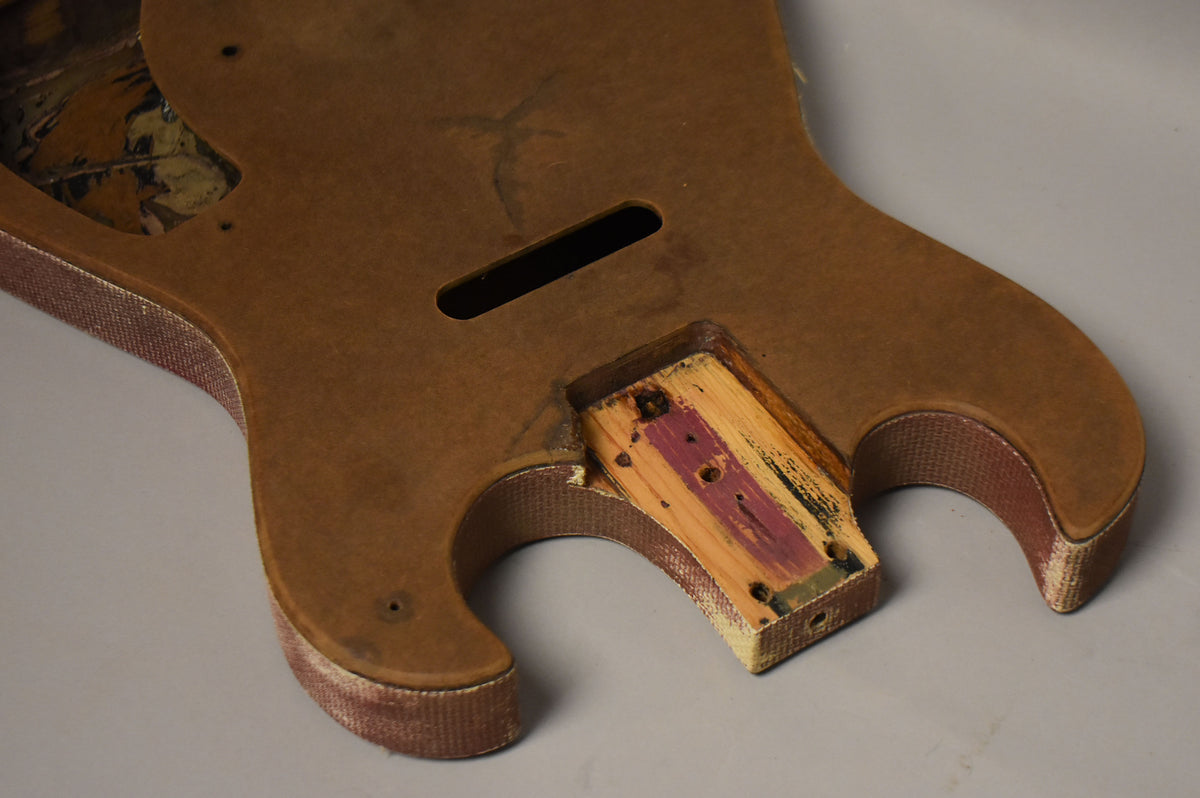 The guitar body is a worn, dark brown with red fabric binding, showing a neck pocket with exposed wood and purple paint.