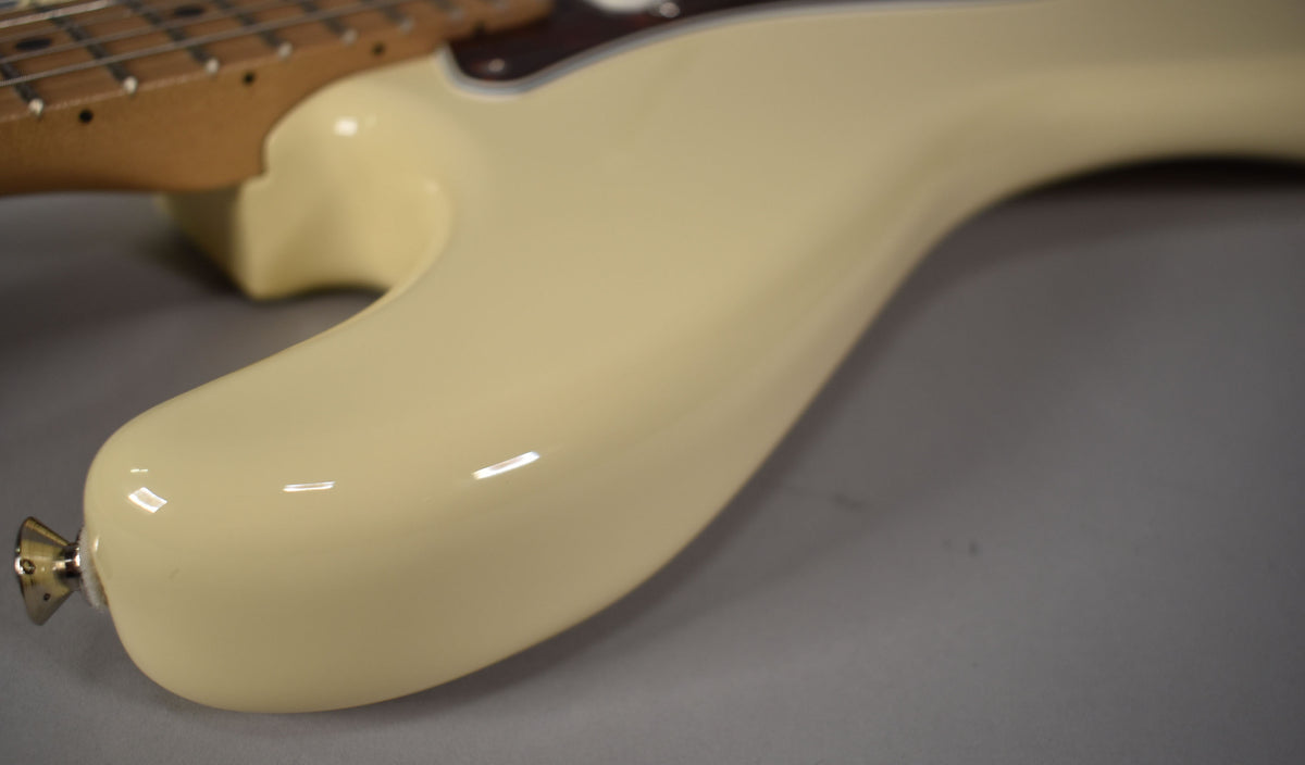 The lower bout of an Olympic White Stratocaster, showing the glossy finish and a chrome strap button at the bottom.