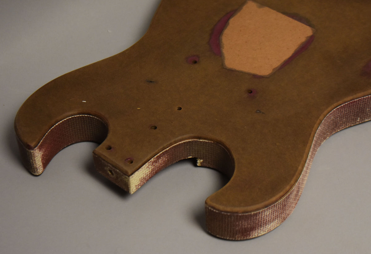 The brown body shows a large rectangular pickup cavity, several screw holes, and wear to the textured red and white side binding.