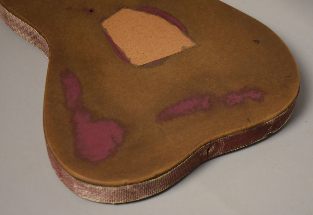 The guitar body's brown top has faded pink areas, a rectangular cutout, and a worn red fabric side binding with exposed wood.