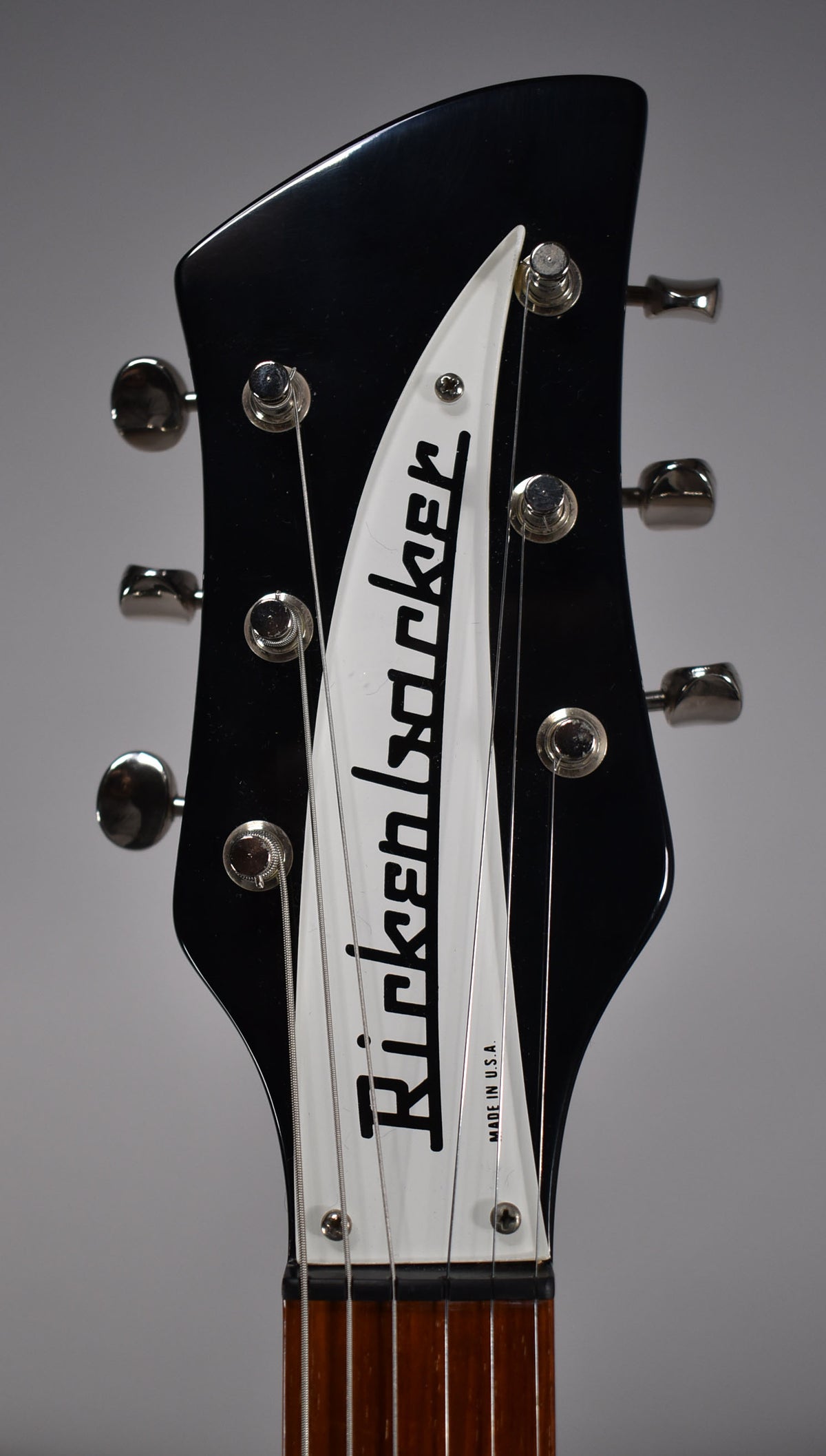 Close-up of the glossy black headstock with a white triangular truss rod cover, showing six chrome tuners and strings.