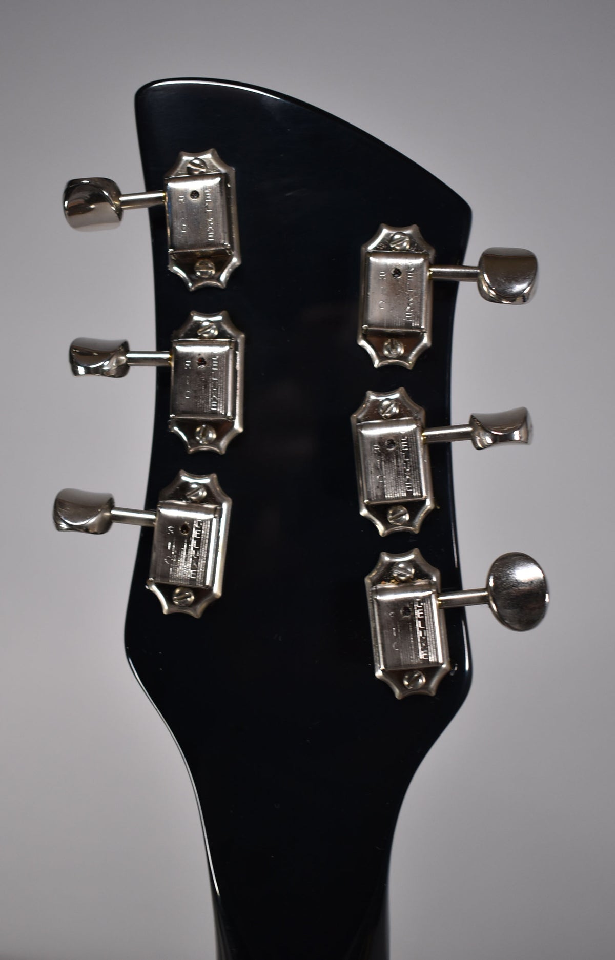 The back of a glossy black headstock with six chrome tuners, three on each side, showing light wear and minor scratches.
