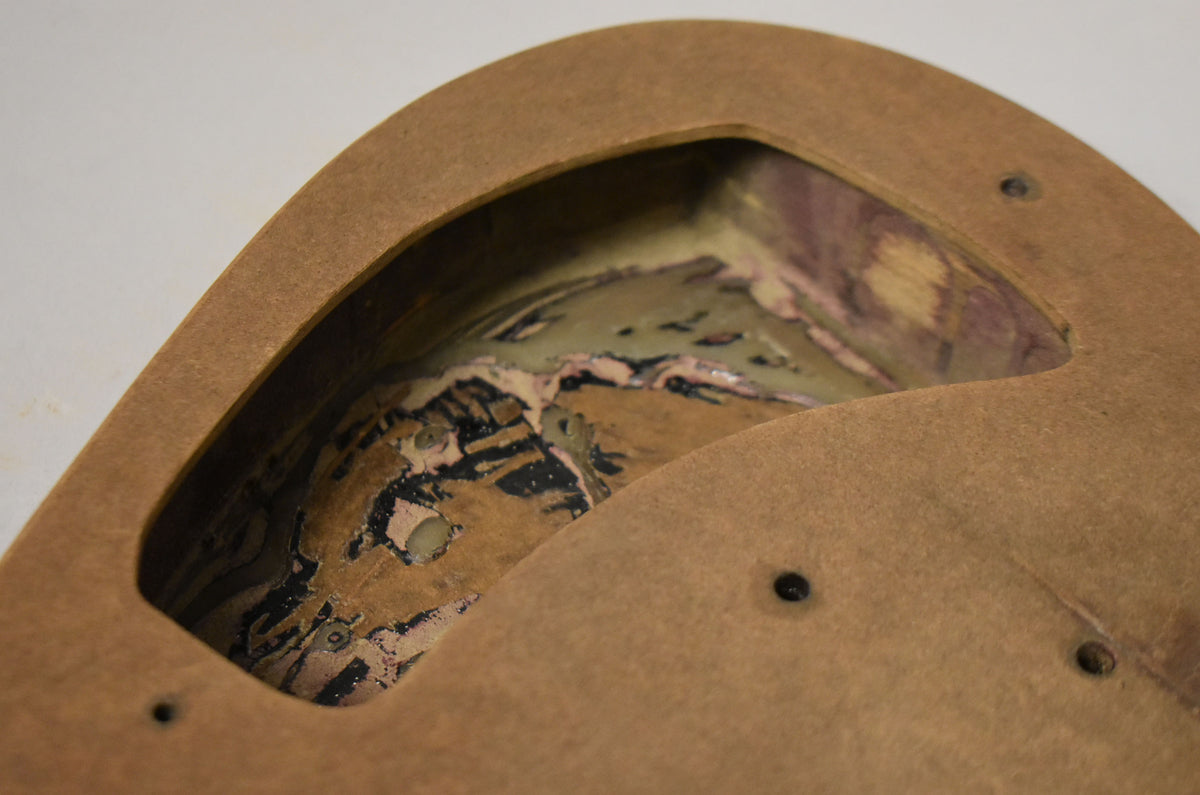 Close-up of the body's control cavity, revealing a worn, multi-layered finish with black, pink, and green paint over wood.