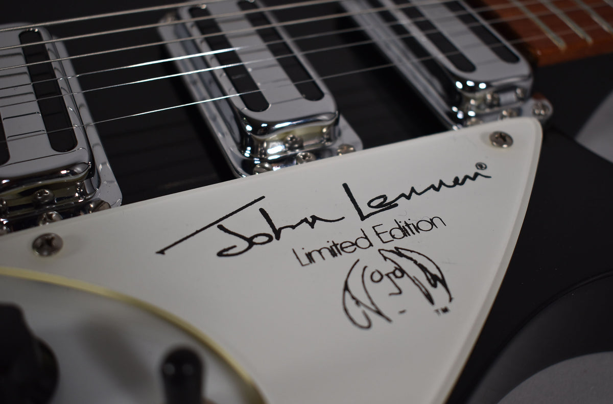 Close-up of a black guitar's white pickguard, showing "John Lennon Limited Edition" and a caricature, with chrome pickups above.