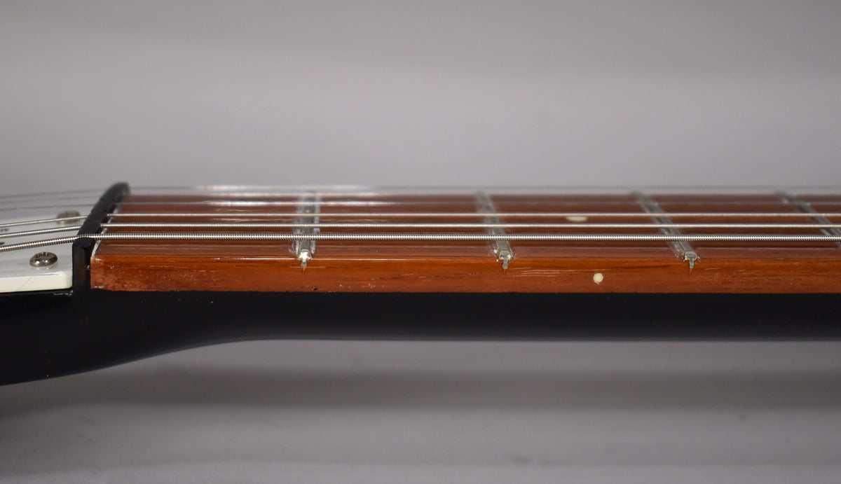A close-up of a guitar's fretboard and strings, showing the nut, frets, and a small white dot inlay.