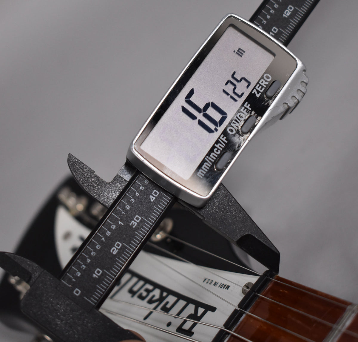 A digital caliper measures the guitar nut, displaying "1.6125 in" on its screen, with "Rickenbacker" visible on the pickguard.